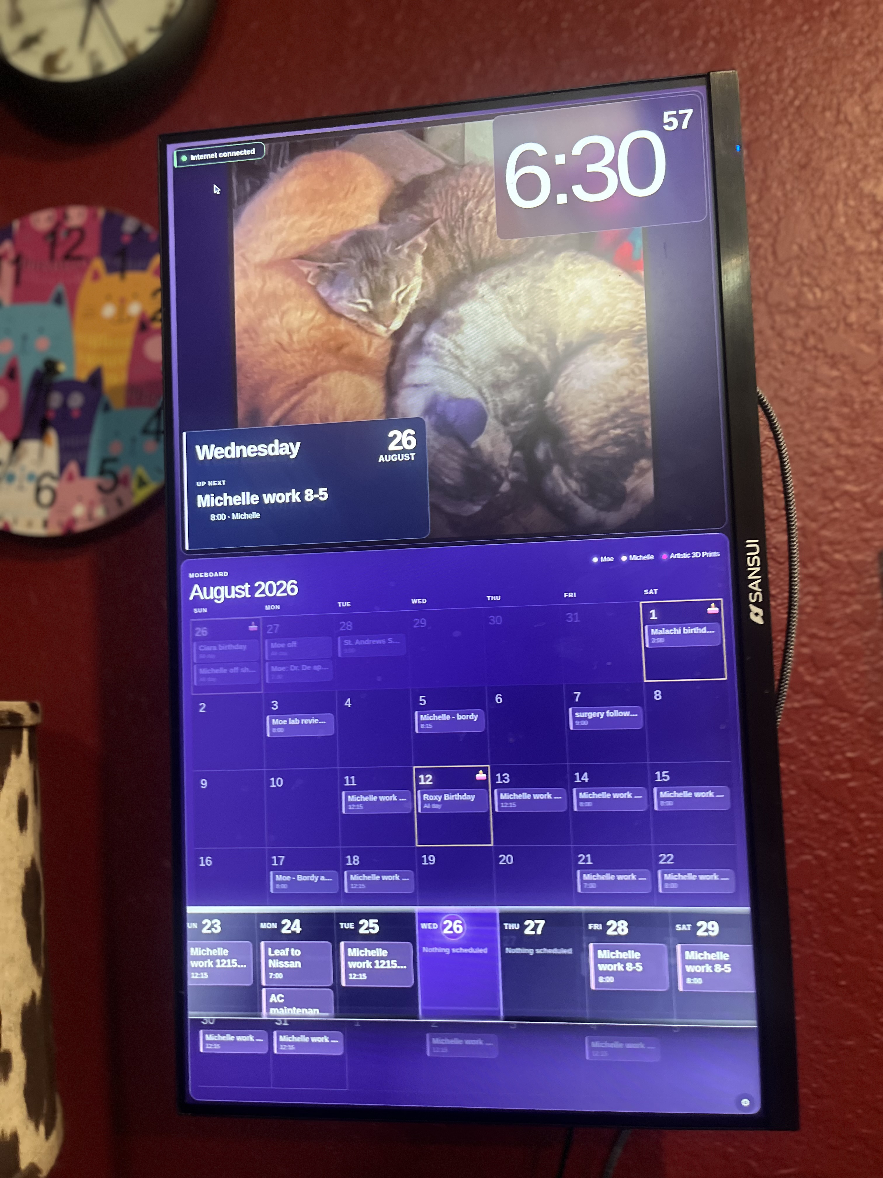 The real MoeBoard family calendar and photo display running on a wall-mounted portrait monitor.